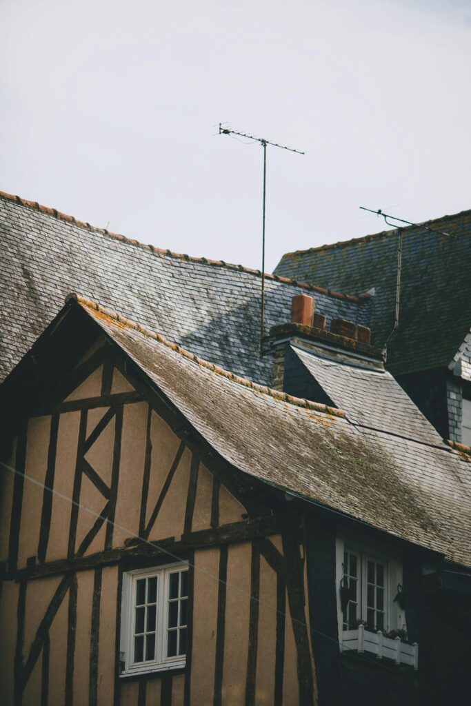 Old dwelling building facades with fenced windows and chimney with antennas on weathered roofs in town
